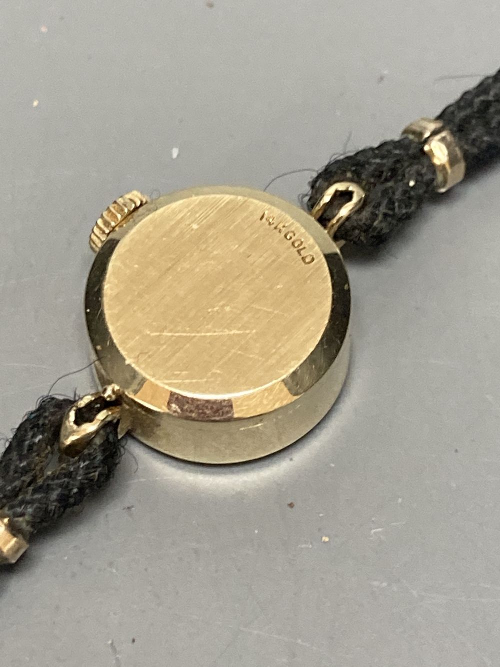A ladys 14k Omega manual wind wrist watch, on twin strand fabric strap, case diameter 13mm ex. crown, gross 7 grams.